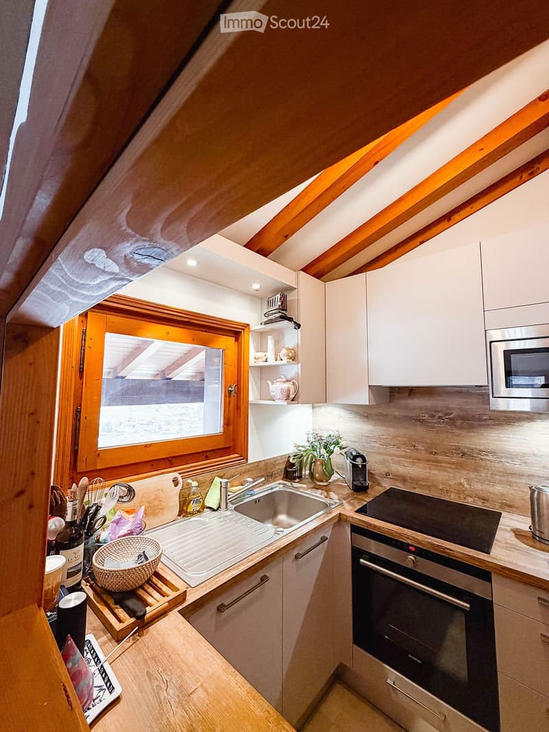 Modern kitchen with white cabinets, stainless steel appliances, and wooden accents. Features a sink, oven, microwave, and various kitchen items on the counter.