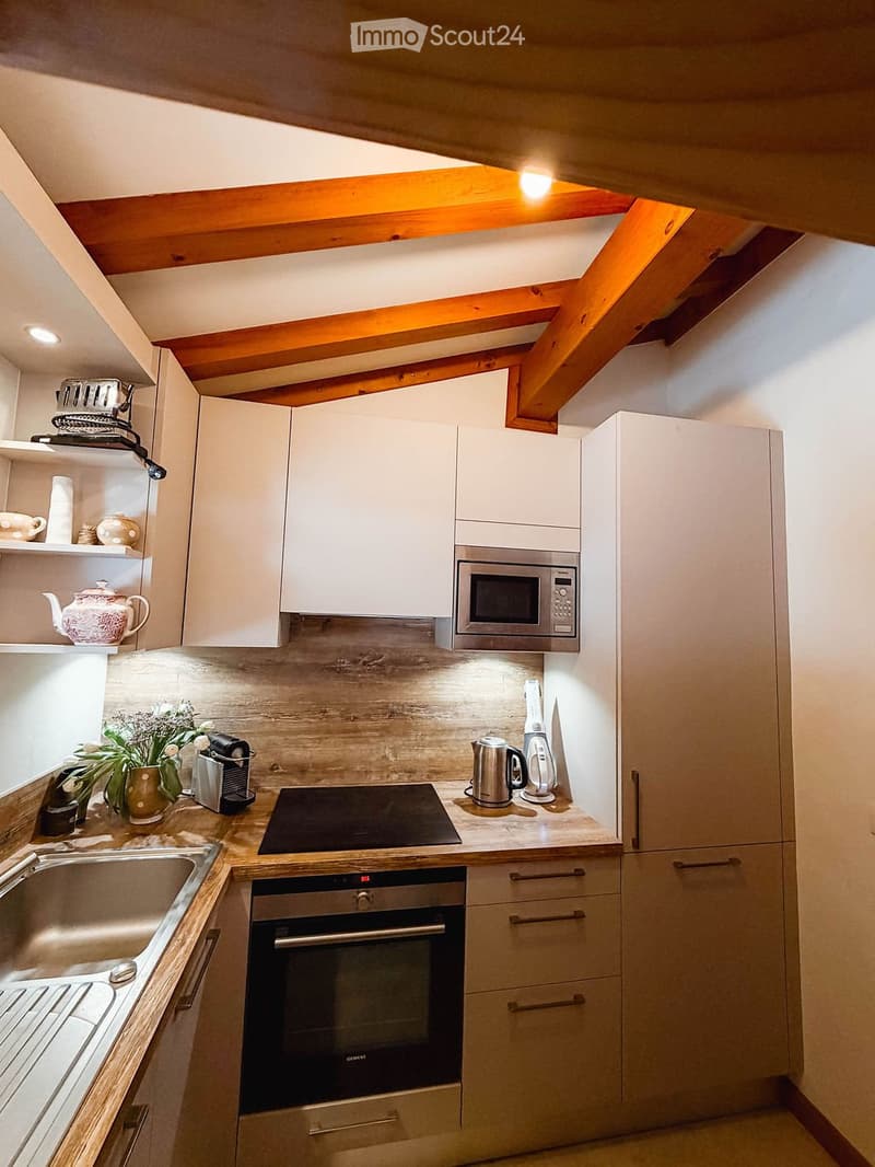 Modern kitchen with white cabinets, stainless steel appliances, wooden countertops, and exposed wooden beams on the ceiling.