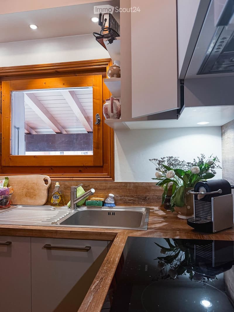 Modern kitchen with wooden countertops, stainless steel sink, coffee maker, and decorative vase with flowers. Features built-in cabinets and a window with wooden frame.
