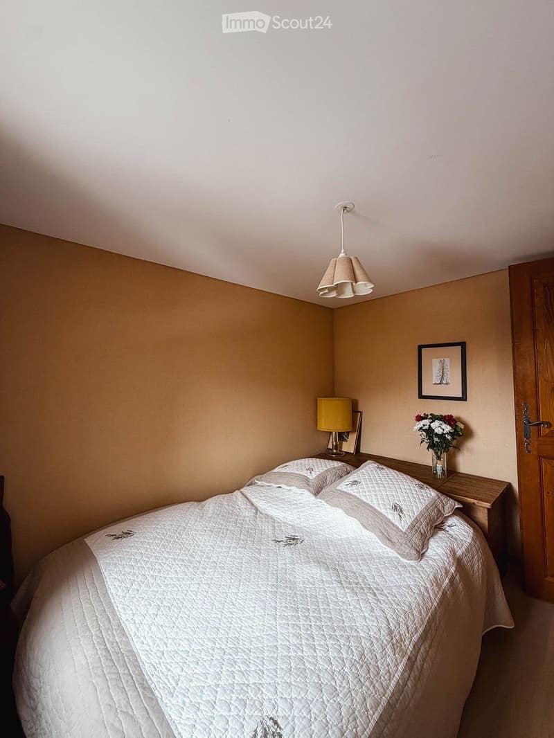 Cozy bedroom with a neatly made bed, nightstand, lamp, picture frame, and a vase with flowers.