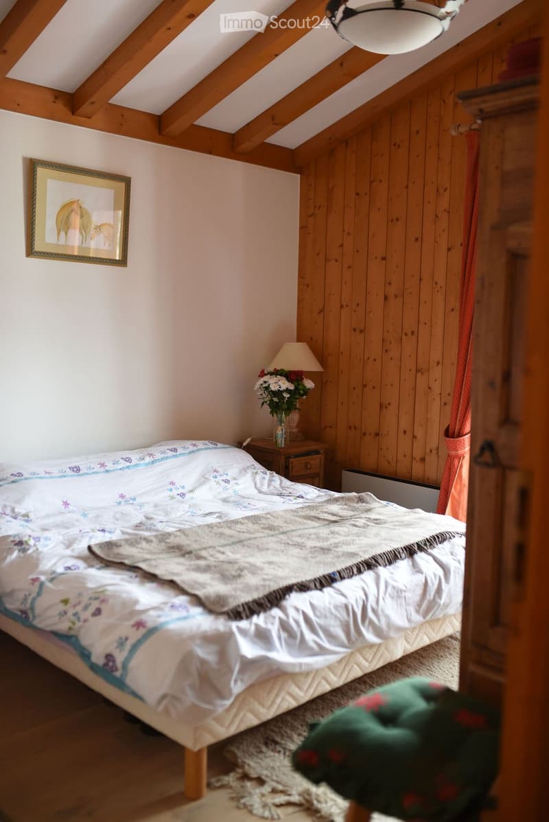 Cozy attic bedroom with wooden walls and slanted ceilings, featuring a bed with a patterned quilt, a nightstand with a lamp, and a vase of flowers on the nightstand.
