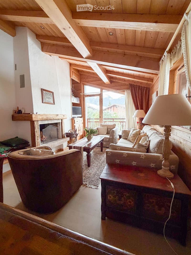 Cozy living room with wooden beams, fireplace, large windows offering a scenic view, and comfortable seating including a sofa, armchair, and coffee table.