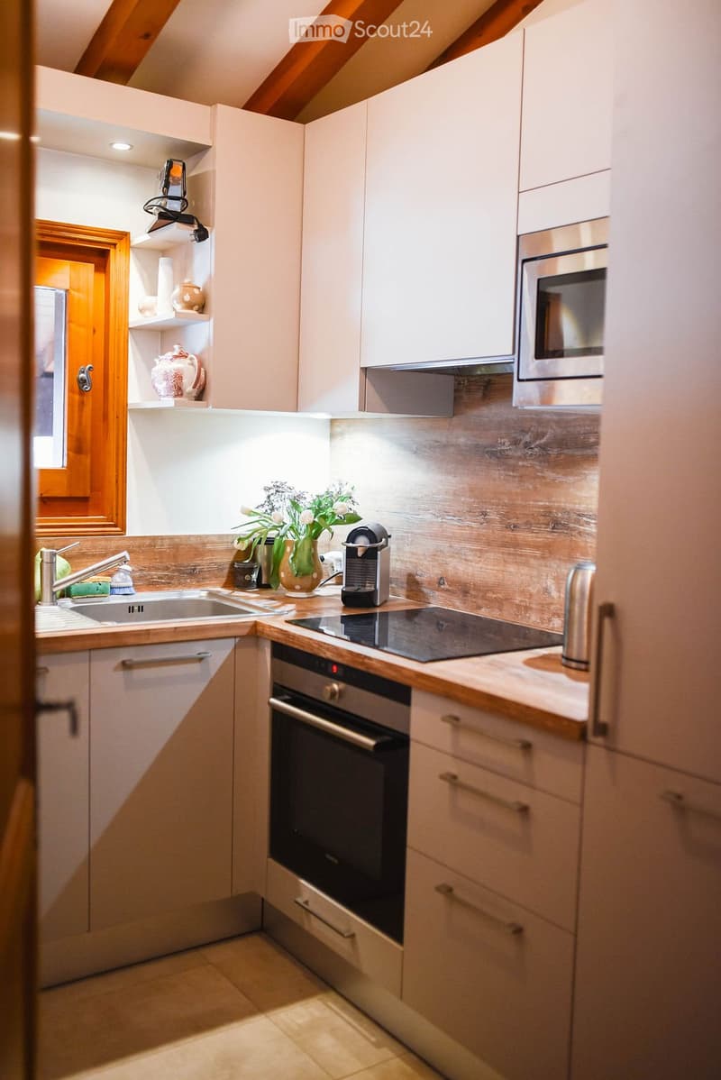 Modern kitchen with light wooden cabinets, stainless steel appliances, and a wooden countertop. Features include a sink, faucet, oven, microwave, coffee maker, and decorative vase with flowers.