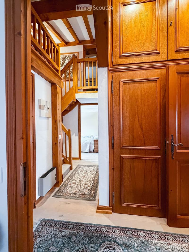 A well-lit hallway with wooden stairs, wooden doors, and patterned rugs on the floor.