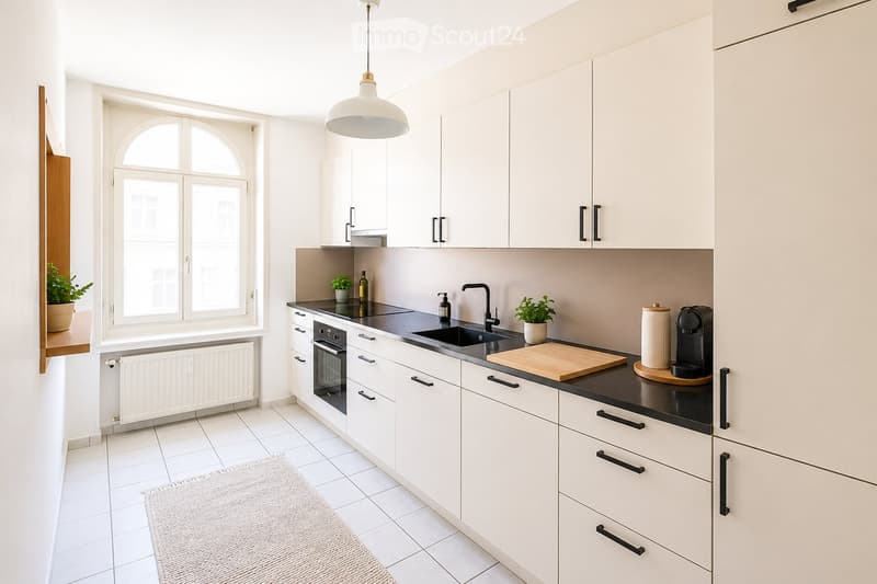 Modern kitchen with white cabinets, black countertops, stainless steel sink, oven, coffee maker, and small potted plants on the counter.