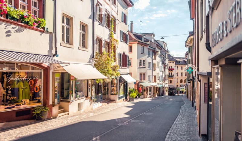 European town street with classic architecture, shops, and flower boxes on buildings.