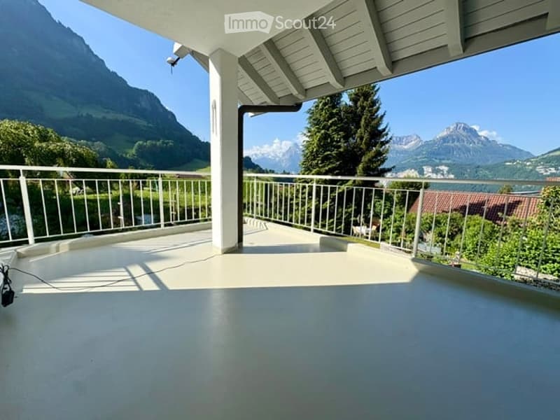 Spacious balcony with white railings, overlooking a scenic mountain landscape and a body of water.