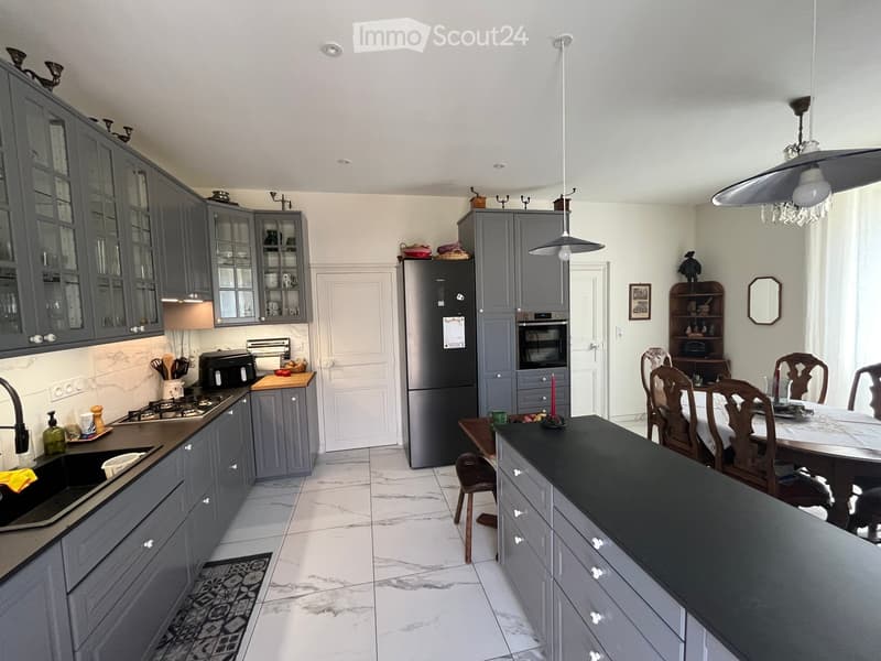 Modern kitchen with grey cabinets, black countertop, stainless steel appliances, and a dining area with wooden chairs and table.