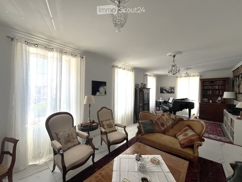 Elegant living room with a cream-colored sofa, wooden coffee table, armchairs, a grand piano, and bookshelves.