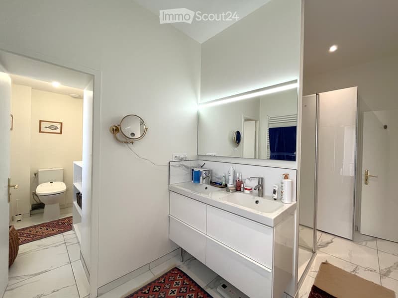 Modern bathroom with white tiles, a double sink vanity, a large mirror, a toilet, and a framed picture on the wall.