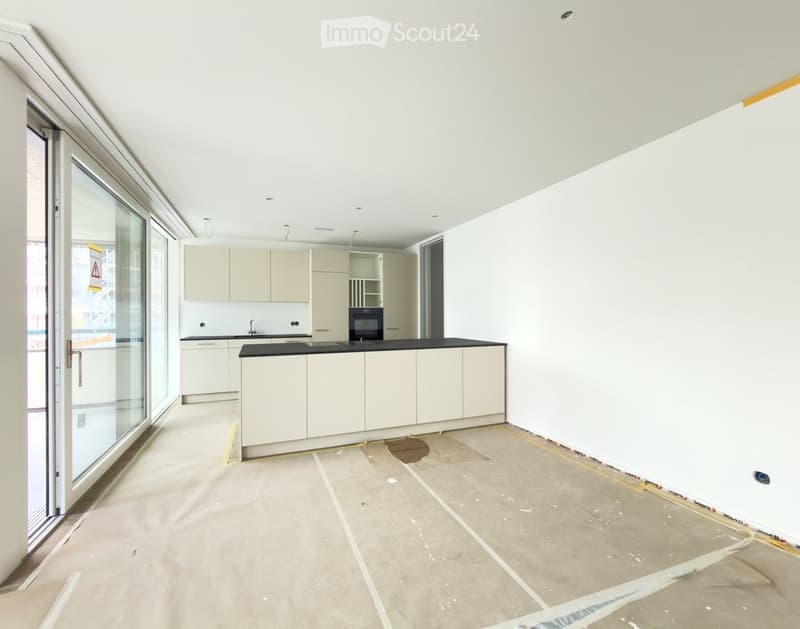 Empty kitchen with white cabinets, a black countertop, and a large glass door leading to a balcony. The floor is unfinished concrete.