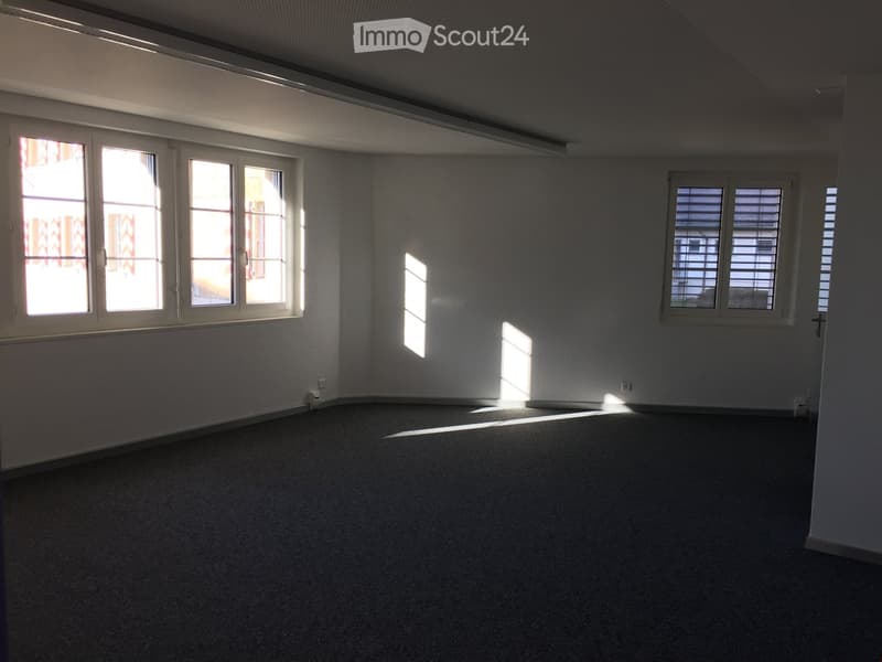 empty room with white walls, black carpeted floor, three windows with white frames and shutters