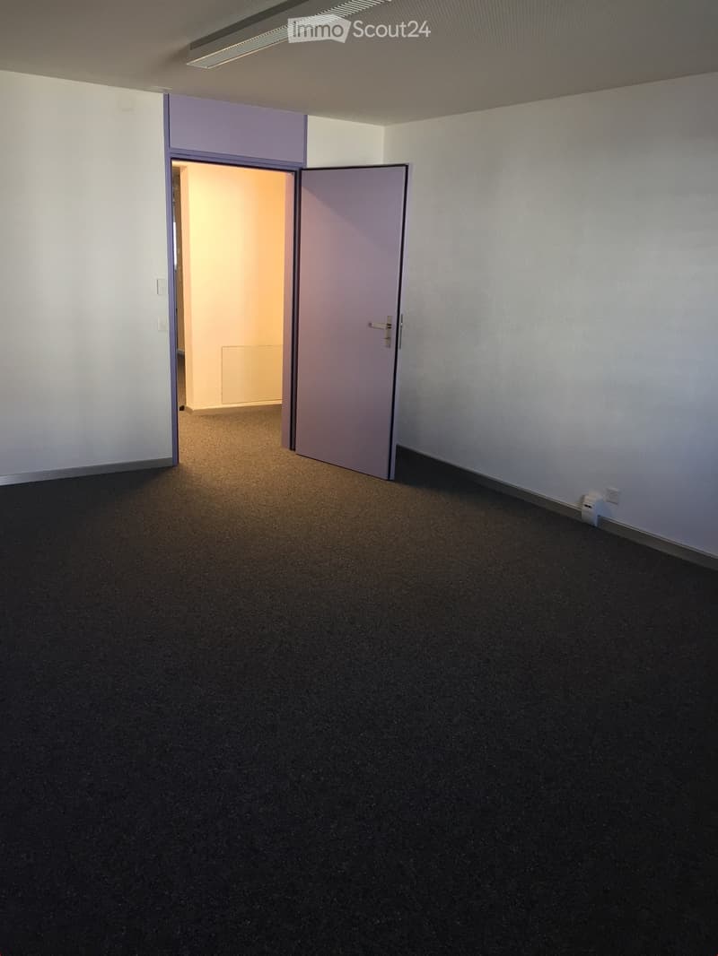 Empty room with white walls, black carpeting, and an open door to another room.