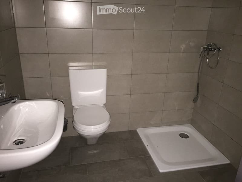 Tiled walls, white ceramic sink, white ceramic toilet, walk-in shower, wall-mounted shower head, no visible features