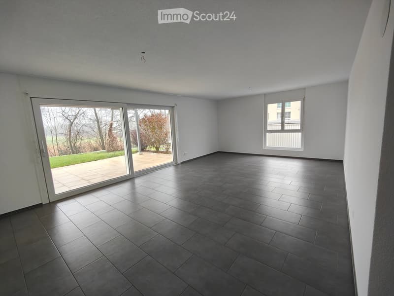 Empty room with dark grey tiled floor, white walls, large sliding glass door leading to outdoor area, and a window on the right side.