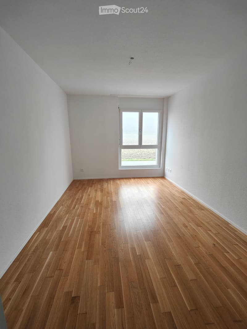 Empty room with light wooden flooring and white walls, featuring a large window with double panes and a door leading outside.