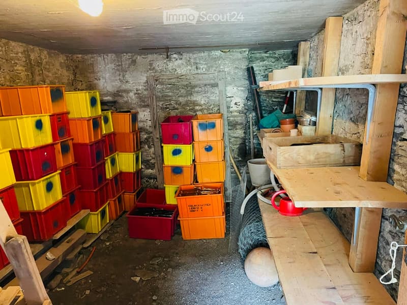 Storage area with stone walls, wooden shelves, and colorful plastic crates stacked on the floor.