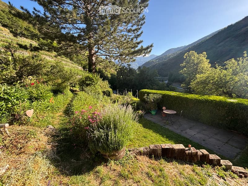 Garden with a small seating area, surrounded by greenery and a scenic mountain view.
