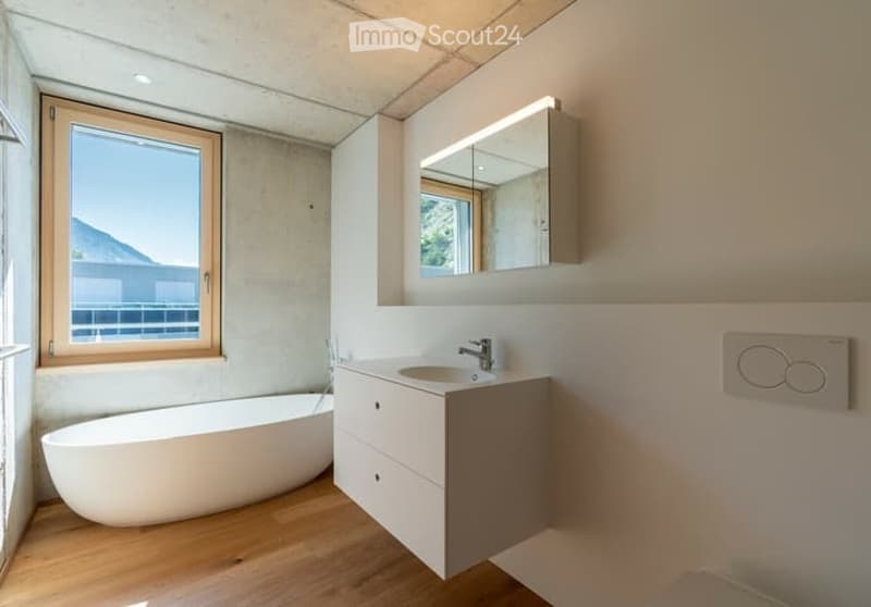 Modern bathroom with a freestanding bathtub, a sink with a cabinet, a mirror, and a large window offering a scenic view.