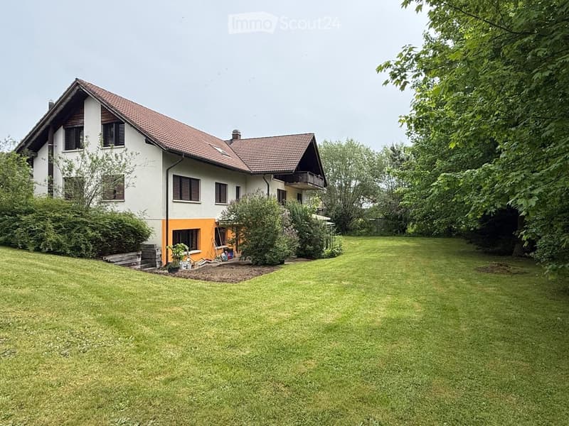 House. Two-story house with a red-tiled roof, white and orange exterior, surrounded by a well-maintained lawn and trees.