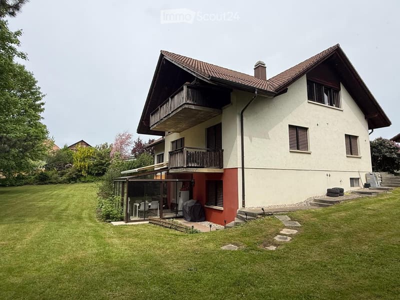 House. Two-story house with a red-tiled roof, balconies, and a well-maintained lawn. The house features a covered patio area with outdoor furniture and a barbecue grill.