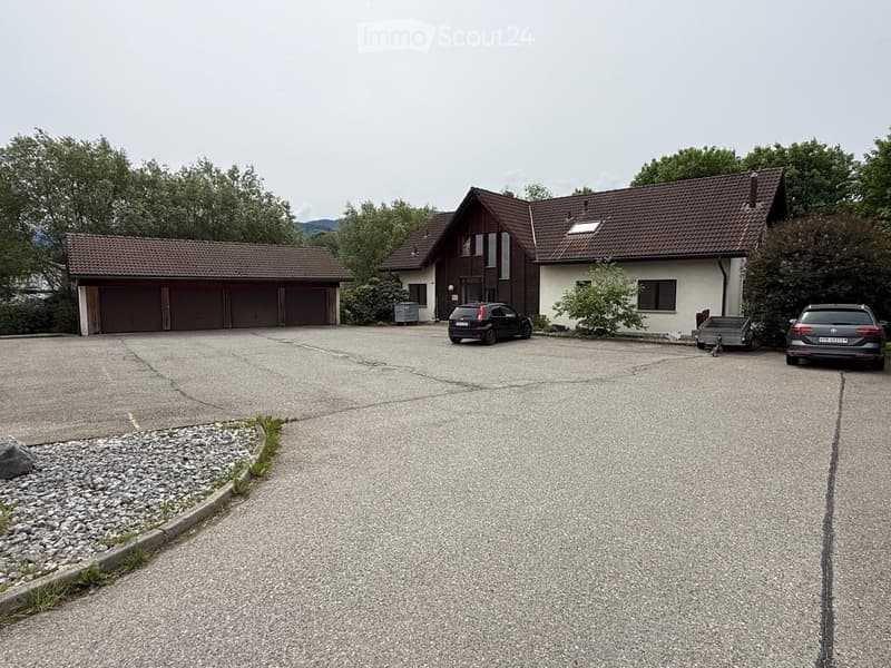 House. Two-story house with a tiled roof, garage, and driveway with parked cars.