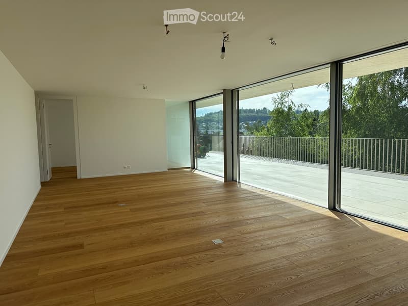 Empty room with wooden flooring, white walls, large sliding glass doors leading to a balcony, and natural light streaming in.