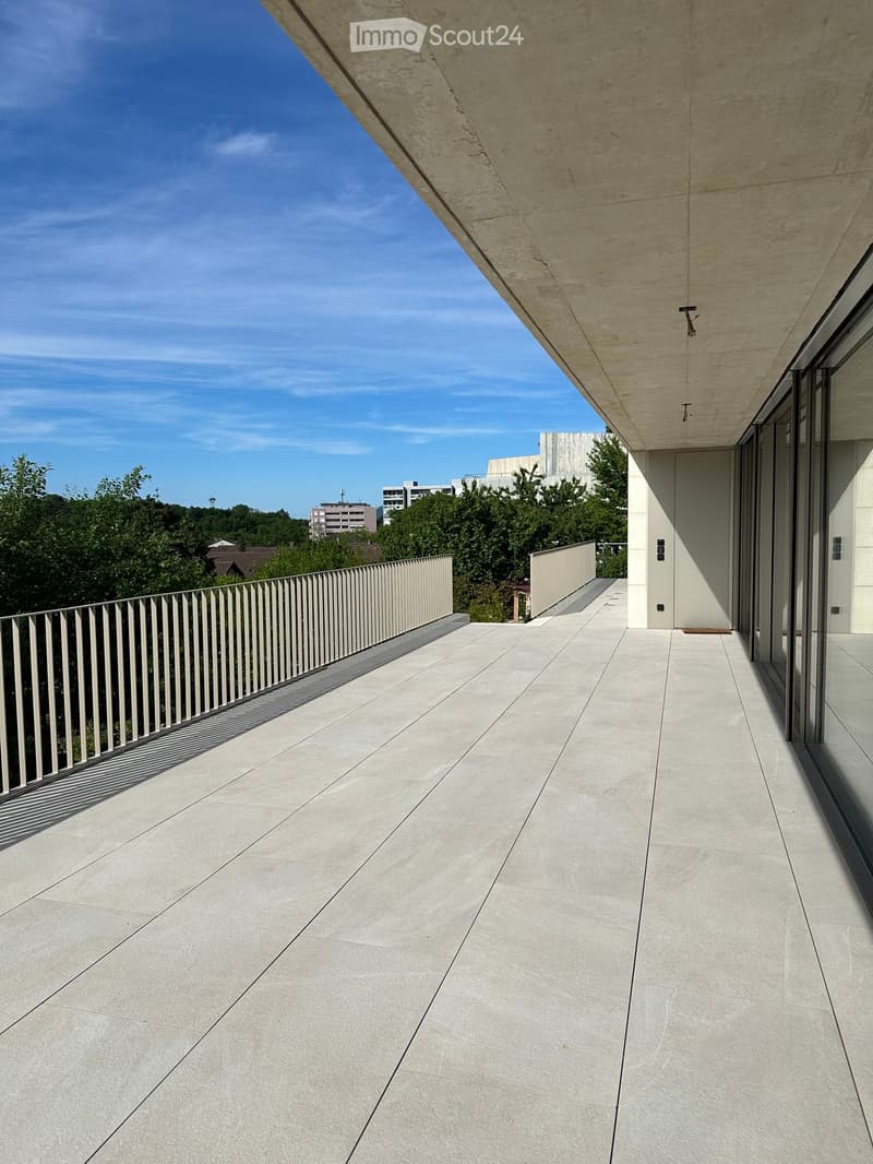 Modern balcony with light-colored concrete tiles, sleek metal railing, and expansive cityscape view.