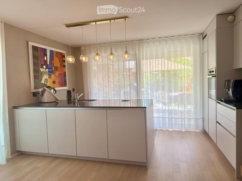 Modern kitchen with white cabinets, a central island, pendant lights, and a large window with sheer curtains. Includes a teapot, coffee maker, and oven.