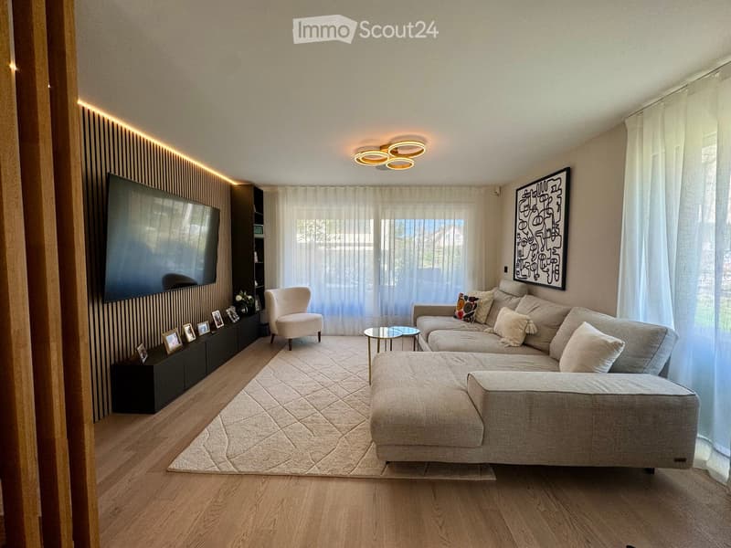 Modern living room with a large sectional sofa, armchair, coffee table, TV mounted on a wooden wall, and decorative picture frames on a black console table.