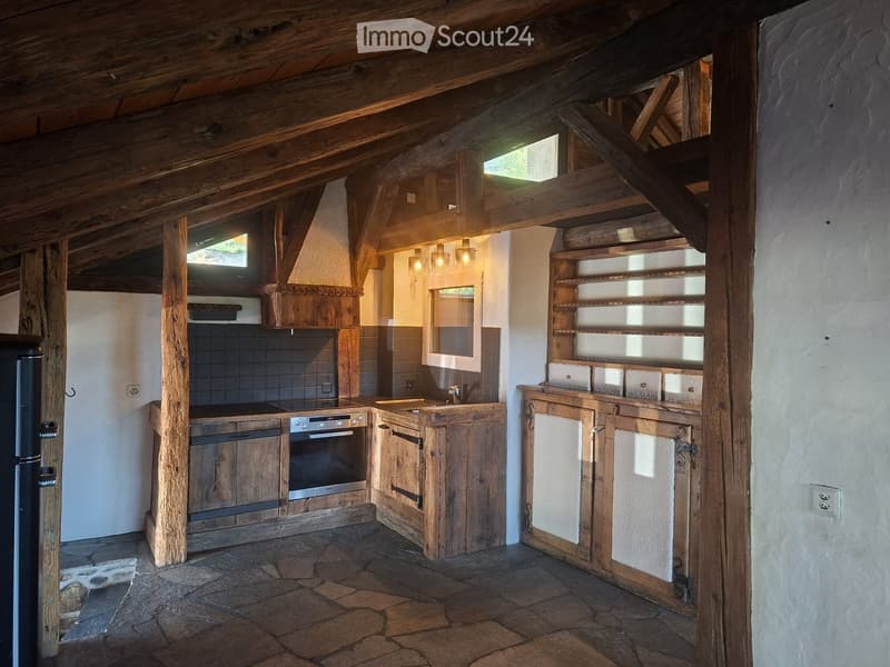 Rustic kitchen with wooden beams, stone floor, wooden cabinets, stainless steel appliances, and open shelving.