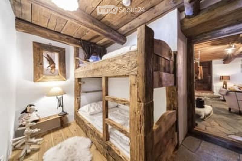 Cozy bedroom with wooden bunk bed, table lamp, framed picture, and a small sitting area with a sofa and rug.