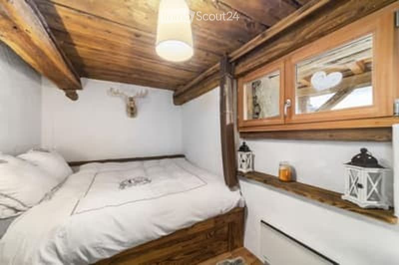 Cozy attic bedroom with wooden beams, a single bed, nightstand, and built-in wooden cabinetry.