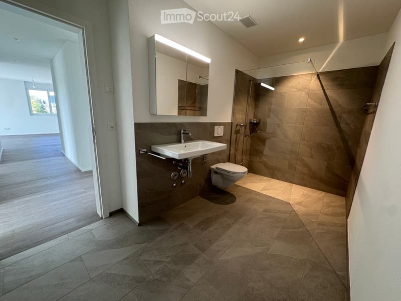 Modern bathroom with a white sink, toilet, large mirror, and glass-enclosed shower area. The space features beige tiles and a sleek design.