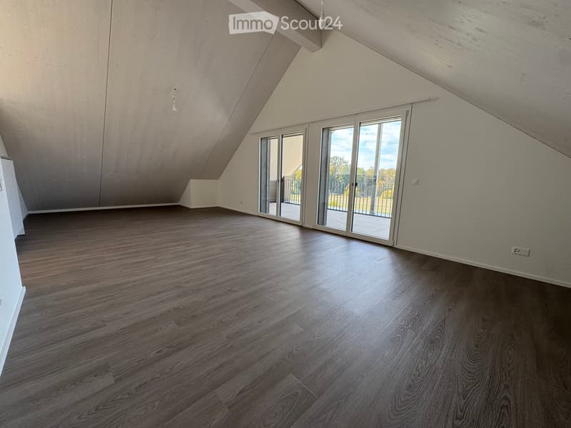 Empty attic room with wooden flooring, large skylight windows, and exposed wooden beams on the ceiling.