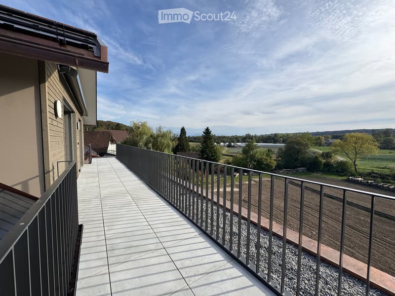 Balcony with metal railing, tiled floor, overlooking a rural landscape with trees and fields.