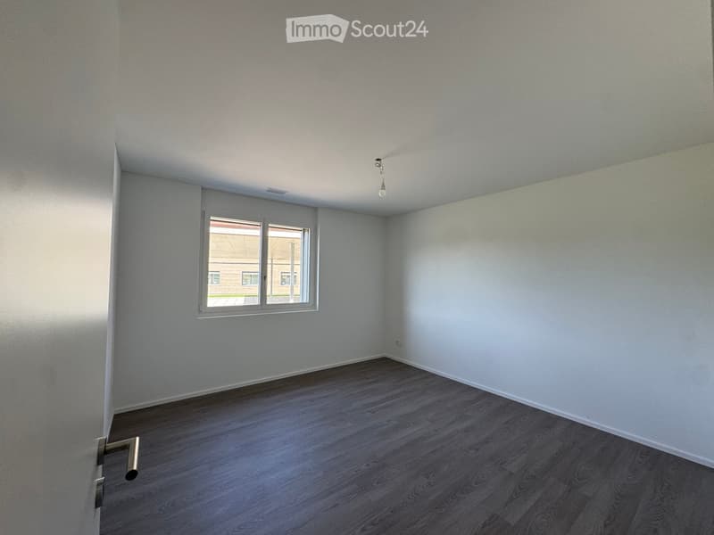 Empty room with light grey walls, wooden flooring, and a single window with white frame. No furniture or equipment present.