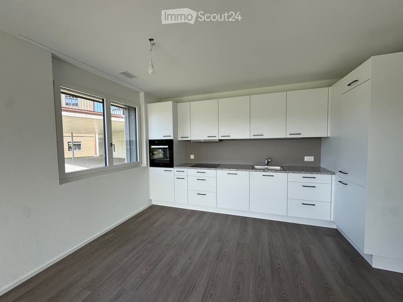 Modern kitchen with white cabinets, dark wooden flooring, and large windows offering a view of the outside.