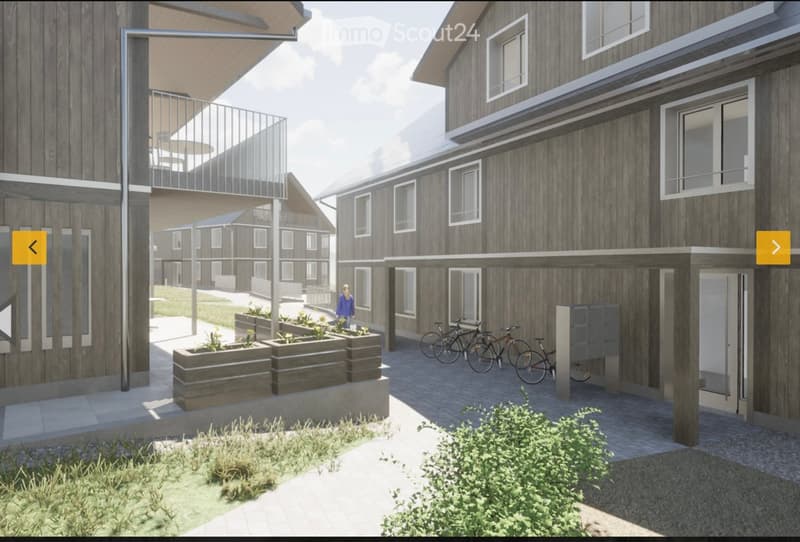 A modern residential building with wooden facades, large windows, and balconies. The courtyard features planters with flowers, bicycles, and a covered walkway.