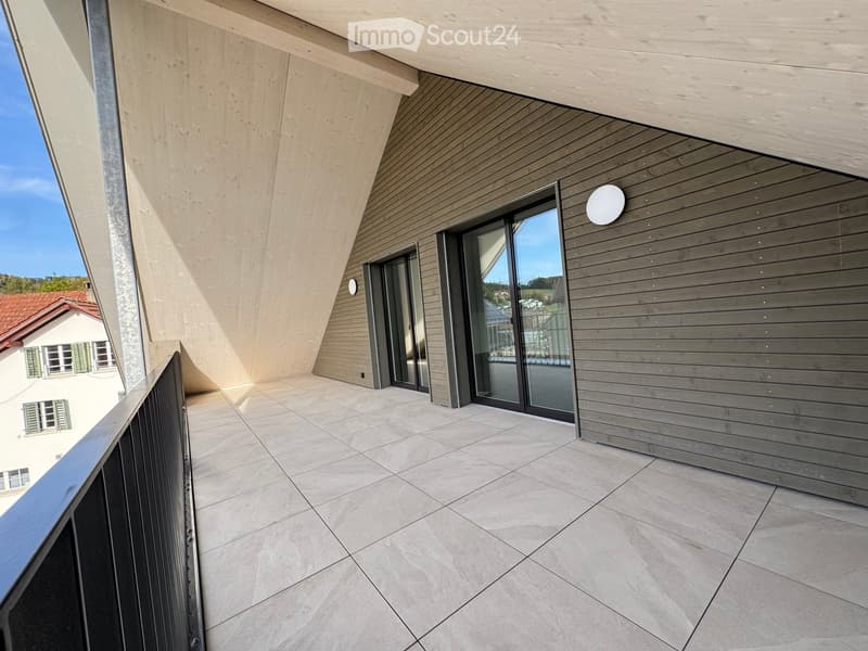 Modern balcony with tiled floor, wooden paneling, large glass sliding doors, and a metal railing.
