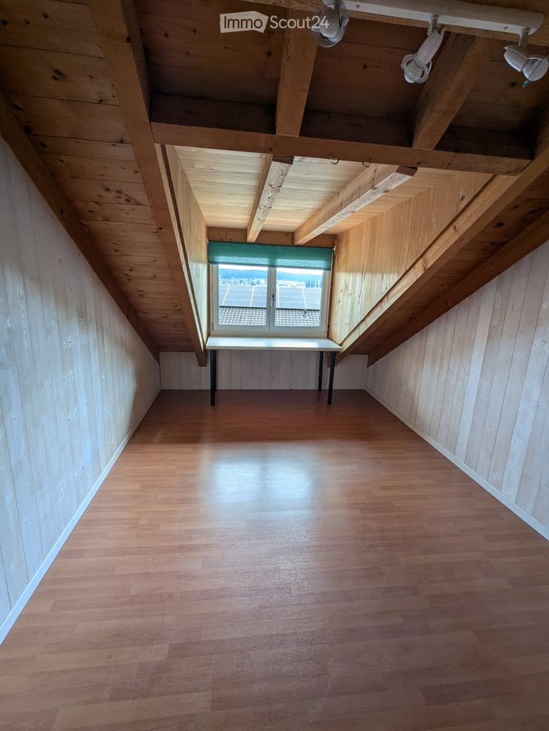 large attic room, wooden floors, sloped ceiling, large skylight window, desk, solar panels outside