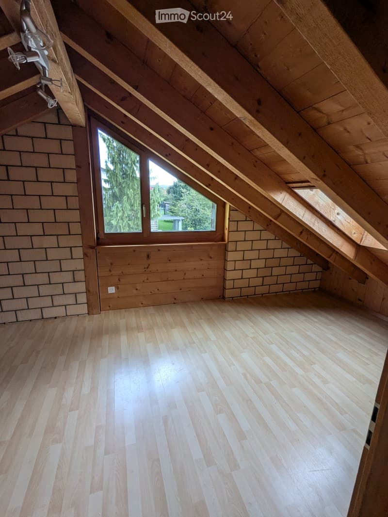 a room in the attic with a window, wood panels, brick walls and wooden floors
