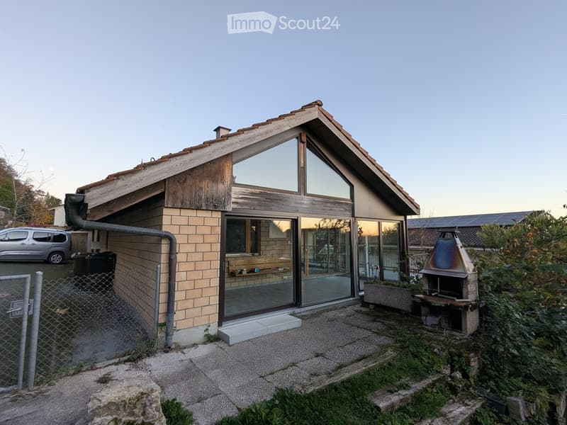 small raised ground floor house, wooden exterior, large glass windows, fireplace, car parked outside, surrounded by vegetation