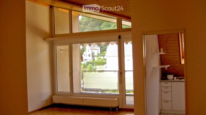Bright, unfurnished room with large windows and a view of the garden and neighboring houses. The room features wooden flooring and white walls.