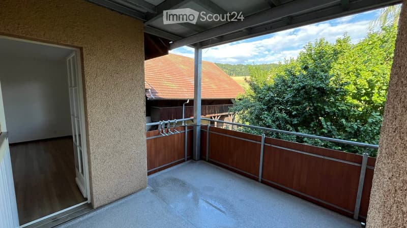 Balcony with wooden railing, concrete floor, and view of a house and greenery.