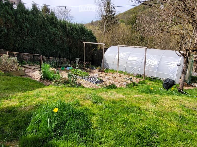 Well-maintained garden with a lawn, raised garden beds, and two greenhouses. The area includes various plants, a tree, and outdoor lighting.