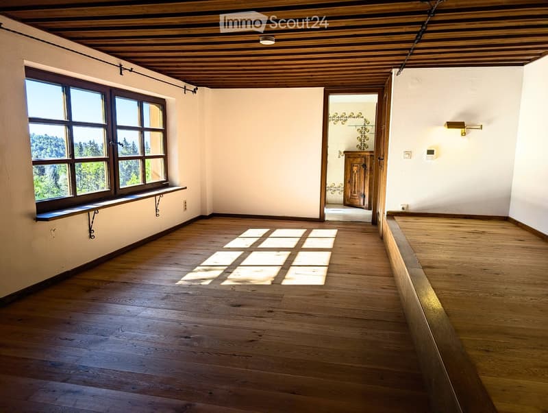 Empty hallway with wooden flooring, white walls, large windows, and a wooden door leading to another room.