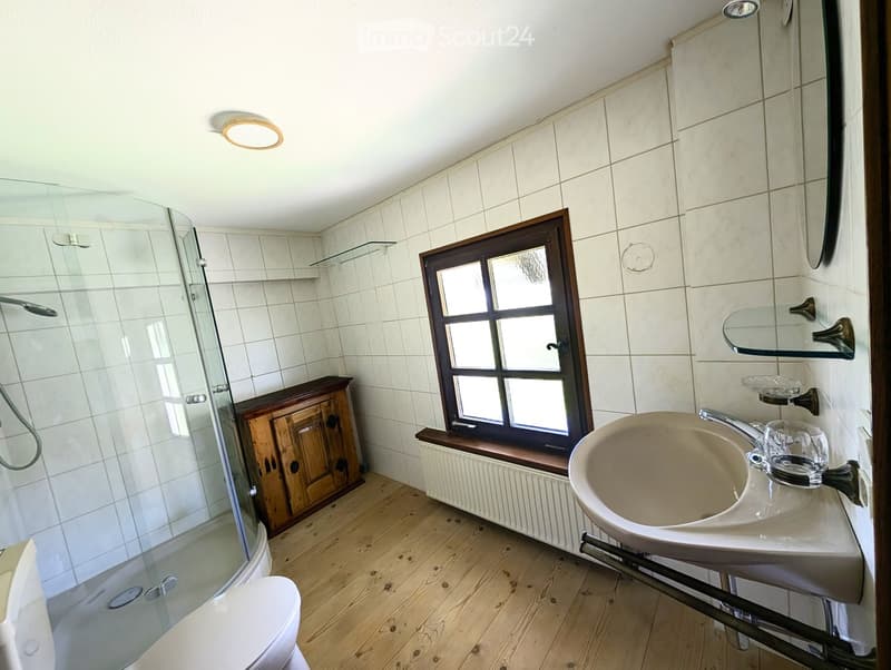 Bathroom with wooden floor, tiled walls, sink, mirror, cabinet, shower, and toilet.