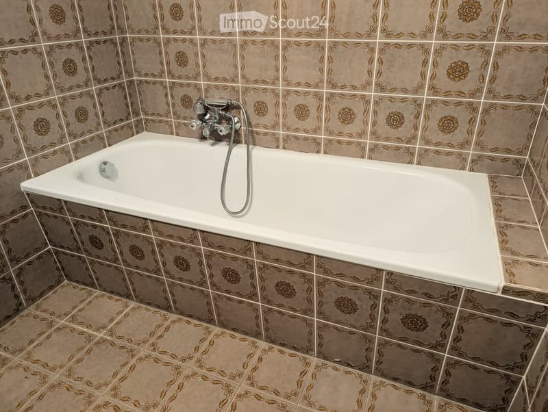 Bathroom with a white bathtub, decorative tiled walls and floor, and a modern faucet with a handheld showerhead.
