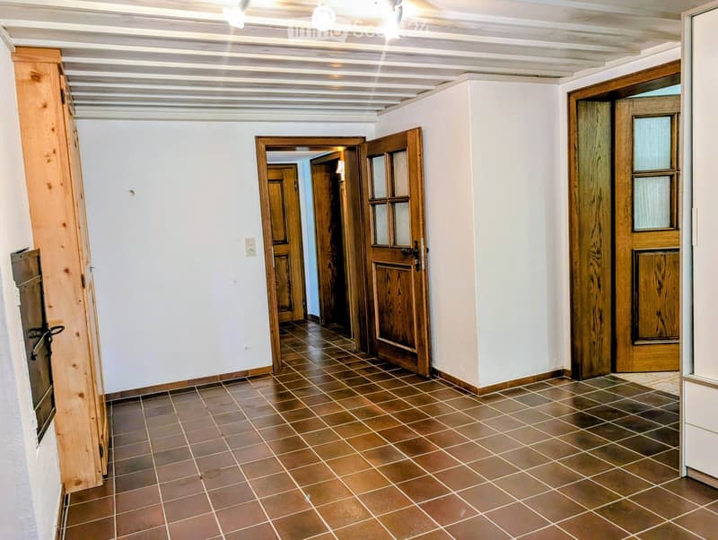 Empty hallway with tiled floor, wooden doors, and white walls.